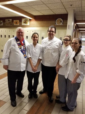 A group of culinary students standing with their instructor in chef uniforms