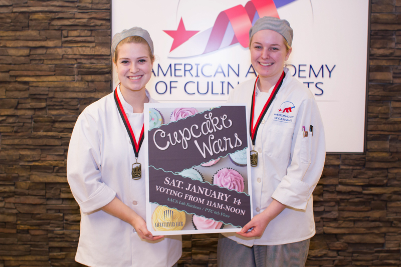 Two culinary students holding a "Cupcake Wars" sign