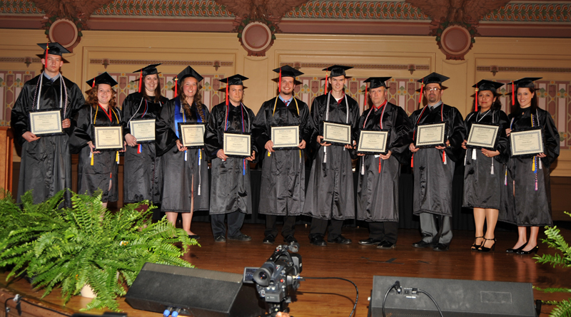 Students standing on stage with diplomas